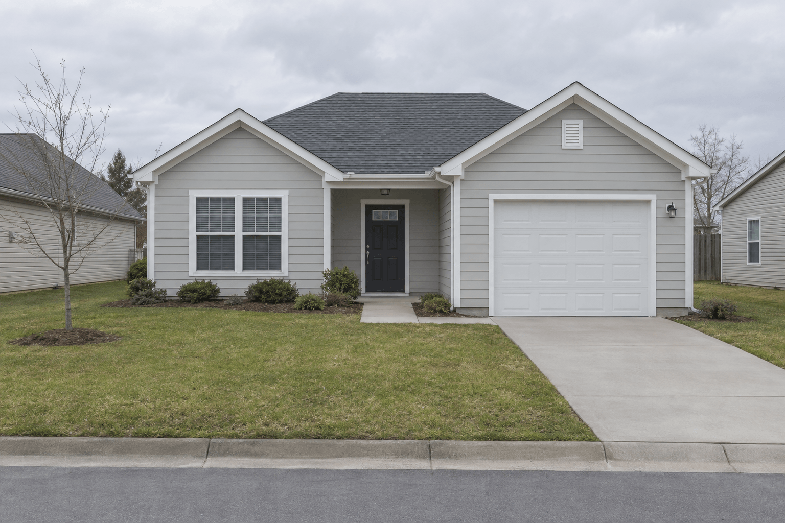 A single-storey single-family rental house with light grey siding and an attached garage under an overcast sky.